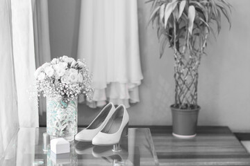 horizontal shot of wedding rings by the window with blowing curtains and some slippers and a white flower arrangement on a glass table