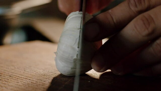 Close up slicing whole garlic bulb in half with sharp knife on wood board