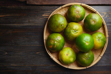 Green tangerine orange fruit in a bamboo basket on wooden background, Table top view
