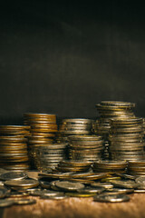 Coins are set up in rows of high and low gradients and coins scattered across the floor in a pattern that are stacked on an old wooden tabletop and black background.