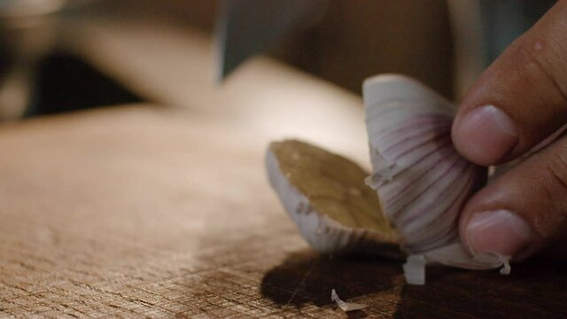 Cutting whole garlic bulb in half on wooden chopping board, close up hands