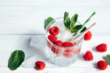 Chilled water, soda, cocktail with raspberries and ice, decorated with mint leaves and cocktail tubes stands on a white wooden table. Summer, seasonal drinks