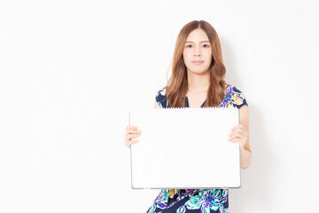Naklejka premium 白い壁の前で、スケッチブックを持っている、青いワンピースを着た若い女性