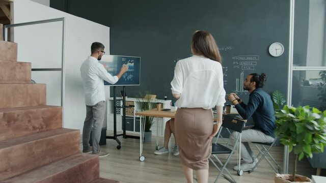 Businesswoman chatting with colleague then watching interactive board presentation sharing ideas with team in modern office. People and job concept.