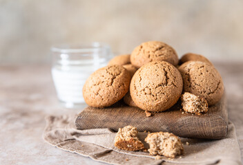 Oatmeal cookies on wooden cutting board with a cup of milk, brown concrete background. Healthy snack or dessert.