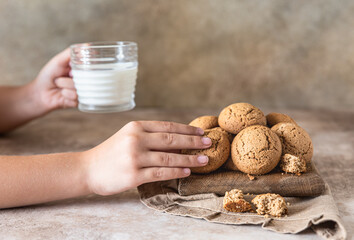 The child's hand takes oatmeal cookies from the board. Brown concrete background. Healthy snack or dessert.