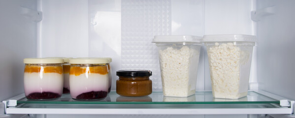 on the glass shelf of the refrigerator, there are cans of yogurt and fruit and grainy cottage...