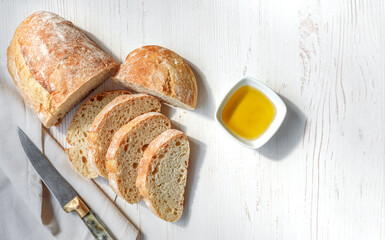 Sliced organic bread ciabatta with vintage linen napkin and bowl of olive oil on white wooden background. Top view of homemade ciabatta with copy space. Flat lay.
