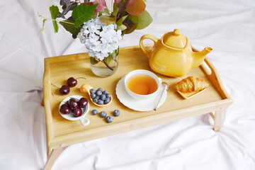 Cup of tea with kettle and berries on the wooden tray. Calm relaxion composition. Cozy atmosphere. Room service in the hotel. Summer time for tea break.