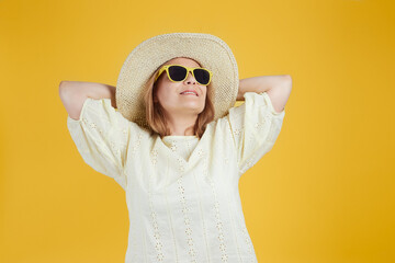 Senior woman in straw hat, sunglasses looking up against bright yellow background