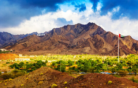 Hatta city welcoming sign written with large letters placed in Hajar mountains and UAE flag flying high in Hatta enclave of Dubai in the United Arab Emirates.