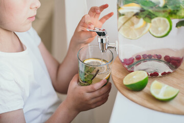 The child himself pours lemonade into a glass. Refreshing summer drink .The kids made their own lemonade for the party. Close-up of the faucet from which lemonade is poured into a glass