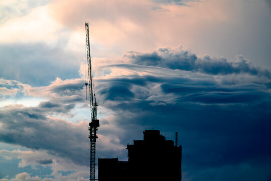 Silhouette of building during construction and construction crane with cloudy background in the evening