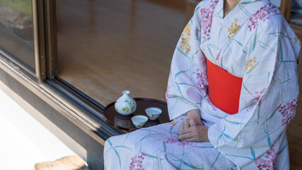 縁側に座る浴衣姿の女性。トレーに乗せた日本酒。日本の夏のイメージ。