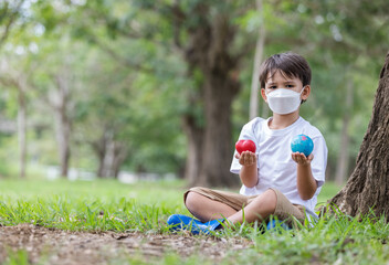 A boy wearing a mask to prevent pollution holding a globe and heart in hand looking at camera .Love health love earth concept