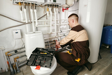 Young male worker in uniform repairing pipes in lavatory