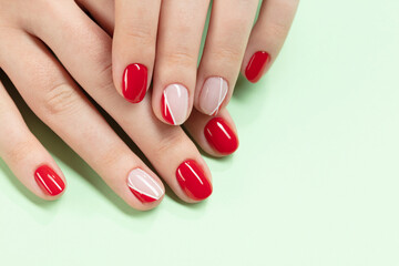 Female hands with new manicure. Hands with pink and red nail polish on a green background. Care for woman hands. Woman in salon receiving manicure by nail beautician. Selective focus
