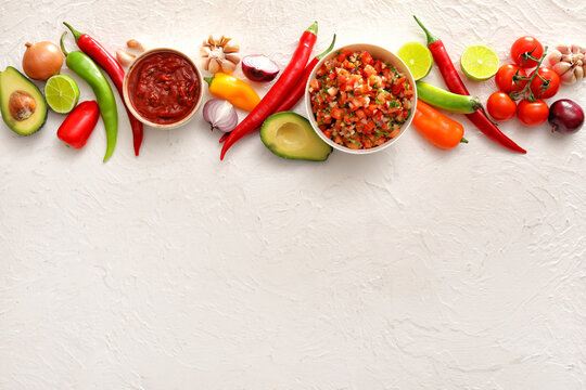 Bowls of tasty salsa sauces with products on white background