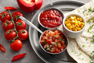 Bowls of tasty salsa sauces with tortilla and corn on grunge background
