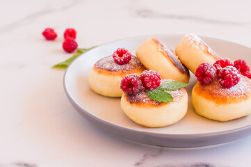 Cottage cheese pancakes, syrniki, curd fritters with fresh raspberries onmarble table.