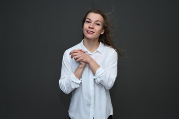 Portrait of a cute caucasian girl with fluttering hair smiling posing on a gray background in a white shirt