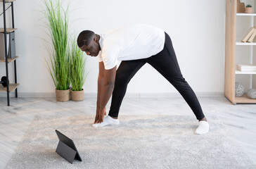 Home training. Happy black man. Online lesson. Enjoying fitness. Concentrated african guy bending...