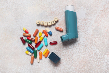 Modern inhaler, pills and word ASTHMA on grunge background