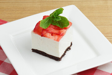 Strawberry cheesecake and fresh strawberries on top served on white plate on a rustic wooden table