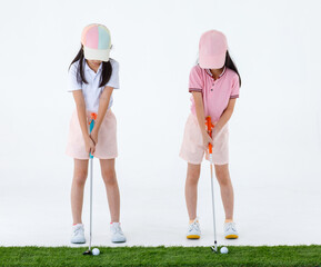 Isolated studio shot of two pretty cute little Asian golfer sister in sport athlete uniform standing together holding putter ready to putting golf ball on green grass in front of white background