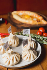 Khinkali cooked on a ceramic plate. Different kinds of Khinkali served on a wooden table, blurred background.