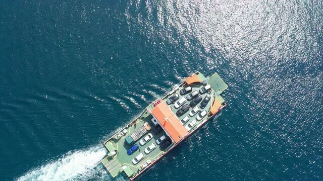 Ferry on the sea, transporting cars: deck of a boat carrying vehicles. Summer sun reflecting off the rippled water surface of lake or river revealing waves texture. Aerial top view from a drone.