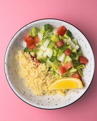 Bulgur with vegetables in a plate over pastel pink background. Delicious healthy dish in a bowl
