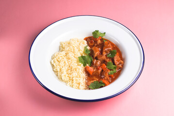 Chicken gravy with rice served in a white plate over pastel pink background.