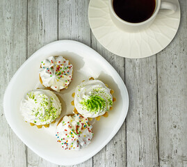 Sponge cake with cream on a white plate, white cup with tea on a light wooden background. Delicious breakfast, afternoon snack, tea party concept. Flat lay. Selective focus.