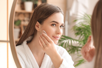 Beautiful young woman applying makeup in bathroom