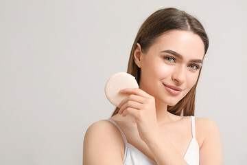 Beautiful young woman with makeup sponge on grey background