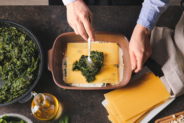 Woman preparing tasty green lasagna in kitchen