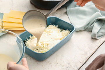 Pouring of sauce into baking dish with green lasagna on table