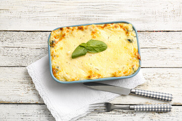 Baking dish with tasty green lasagna on light wooden background