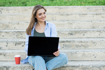 A happy and attractive Caucasian girl is sitting with a laptop on the steps. Distance working. Freelance concept