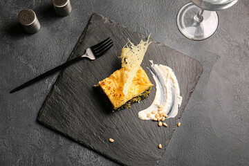 Board with tasty green lasagna on dark background
