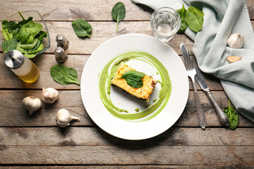 Plate with tasty green lasagna and glass of water on wooden background