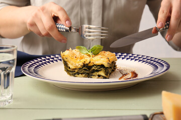 Woman eating tasty green lasagna at wooden table, closeup