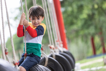 Obraz premium A boy wearing bright colored clothes playing tire swing hanging at playground and having fun healthy summer vacation activity.