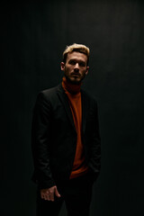 guy on a black background in an orange sweater and leather jacket