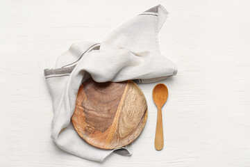Fabric napkin, plate and spoon on light wooden background