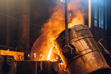 Liquid metal pouring into mold from ladle in foundry metallurgical plant, heavy industry.