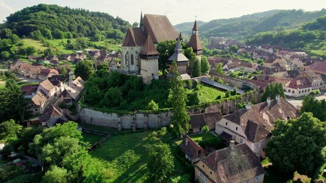 Aerial view of old small Saxon village Biertan in Transylvania, Romania. Fortified church and old houses with orange tiles in the background of green hills. High quality shot, 4K