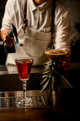woman bartender holds pineapple with burnt brown caramel crust near glass of drink