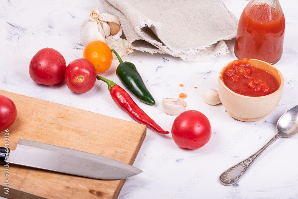 Wall mural Ingredients for making mexican hot sauce - tomatoes, chili and jalapenos, garlic, chopped tomatoes in a cup and ready-made sauce in a bottle on a light background, top view